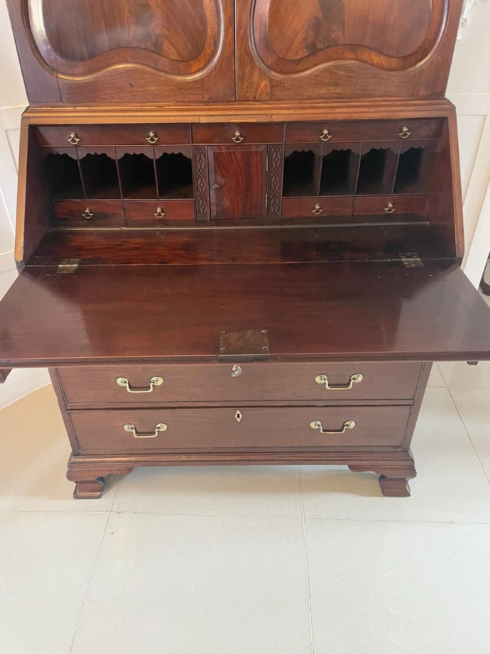 A George II figured mahogany bureau bookcase featuring shaped panel upper doors above a slant-front writing slope and four graduated drawers on bracket feet. View III