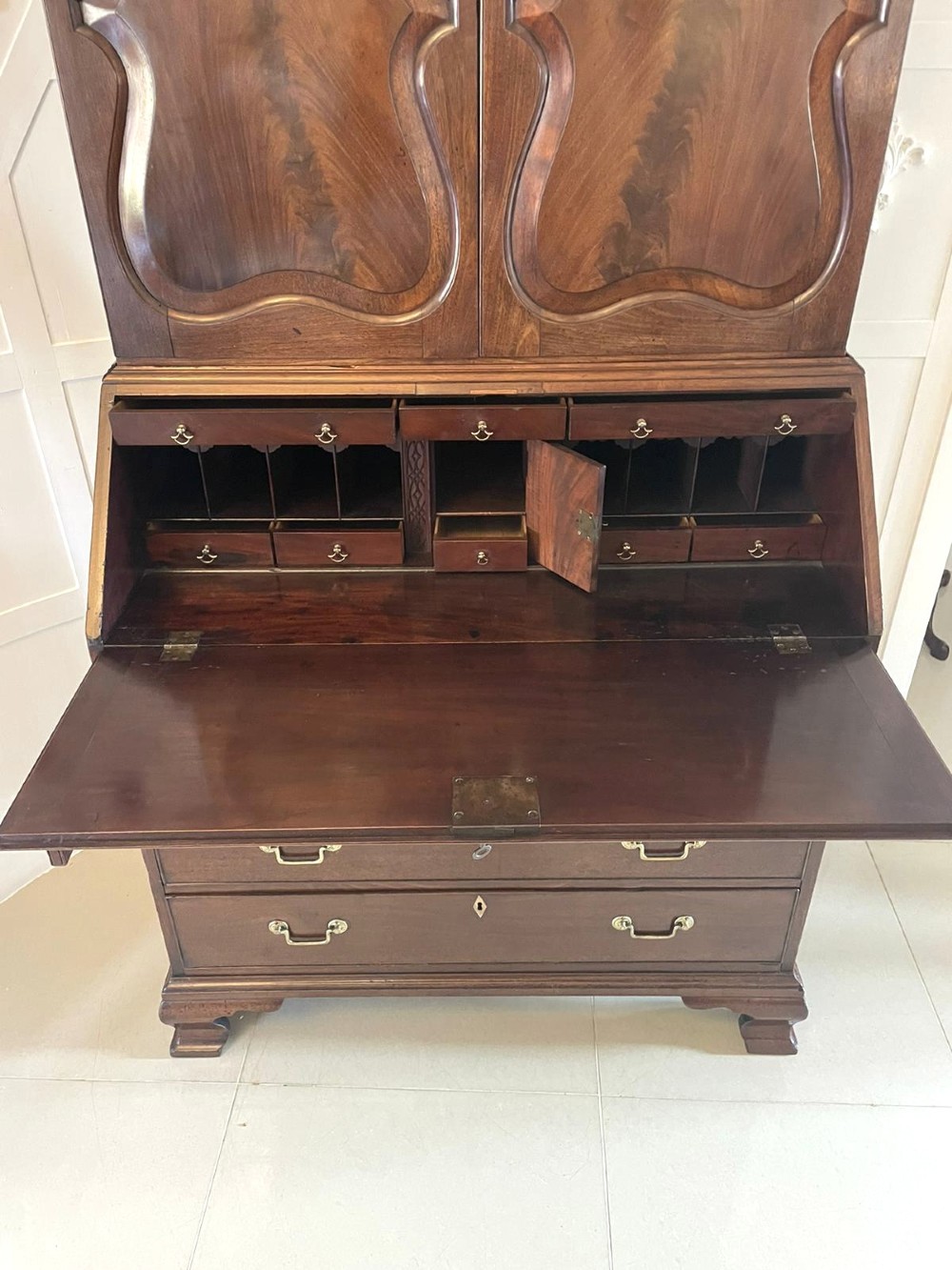 A George II figured mahogany bureau bookcase featuring shaped panel upper doors above a slant-front writing slope and four graduated drawers on bracket feet. View VI