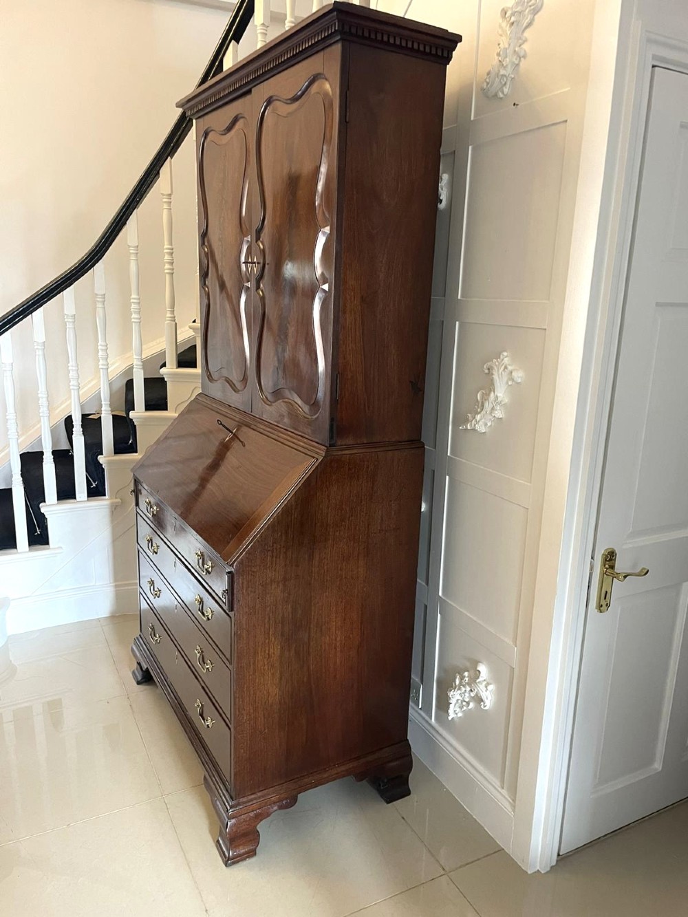 A George II figured mahogany bureau bookcase featuring shaped panel upper doors above a slant-front writing slope and four graduated drawers on bracket feet. View X