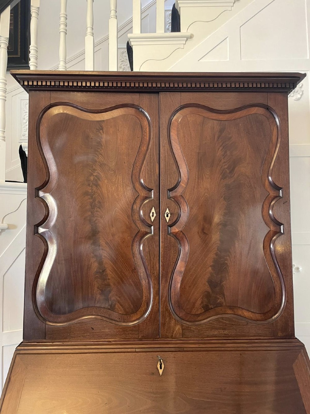 A George II figured mahogany bureau bookcase featuring shaped panel upper doors above a slant-front writing slope and four graduated drawers on bracket feet. View XIII