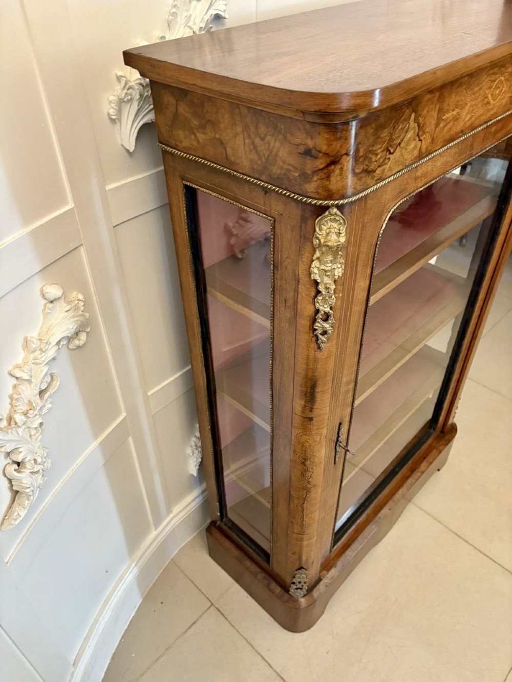 A Victorian burr walnut pier cabinet featuring a single glazed door, floral marquetry along the frieze, and gilt ormolu corner mounts. View VI
