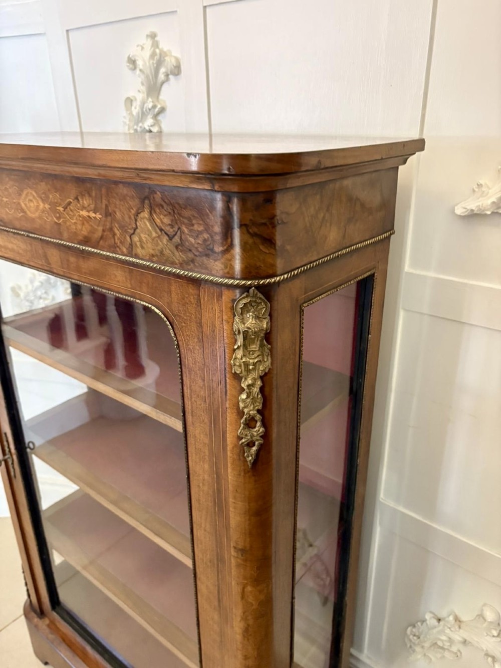 A Victorian burr walnut pier cabinet featuring a single glazed door, floral marquetry along the frieze, and gilt ormolu corner mounts. View IX