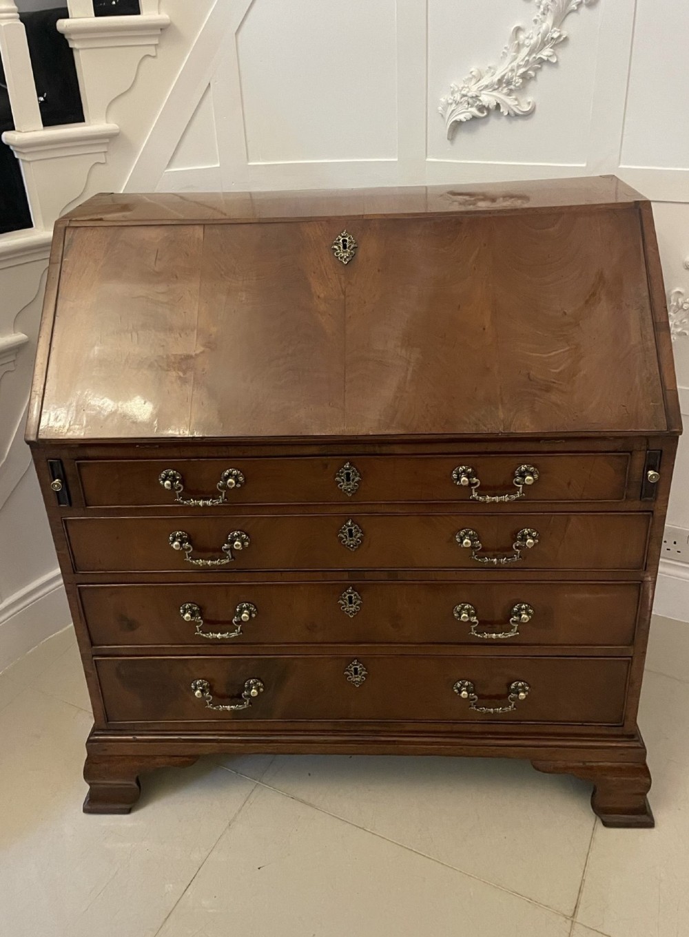 An 18th-century George III mahogany bureau featuring a slant front writing slope above four graduated drawers with brass handles on bracket feet. View IV