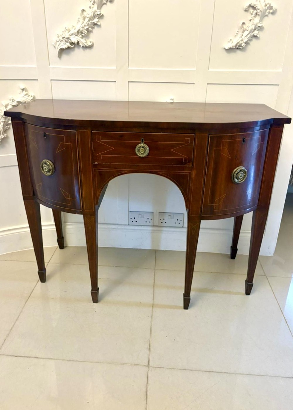 A George III mahogany sideboard featuring geometric boxwood stringing inlay, brass rosette handles, a central arch drawer, and square tapered legs.