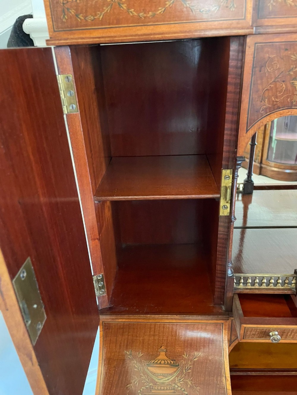 A Victorian inlaid mahogany writing desk featuring a brass gallery top, mirrored arched niche, floral marquetry cabinets, small drawers, and tapered square legs. View II