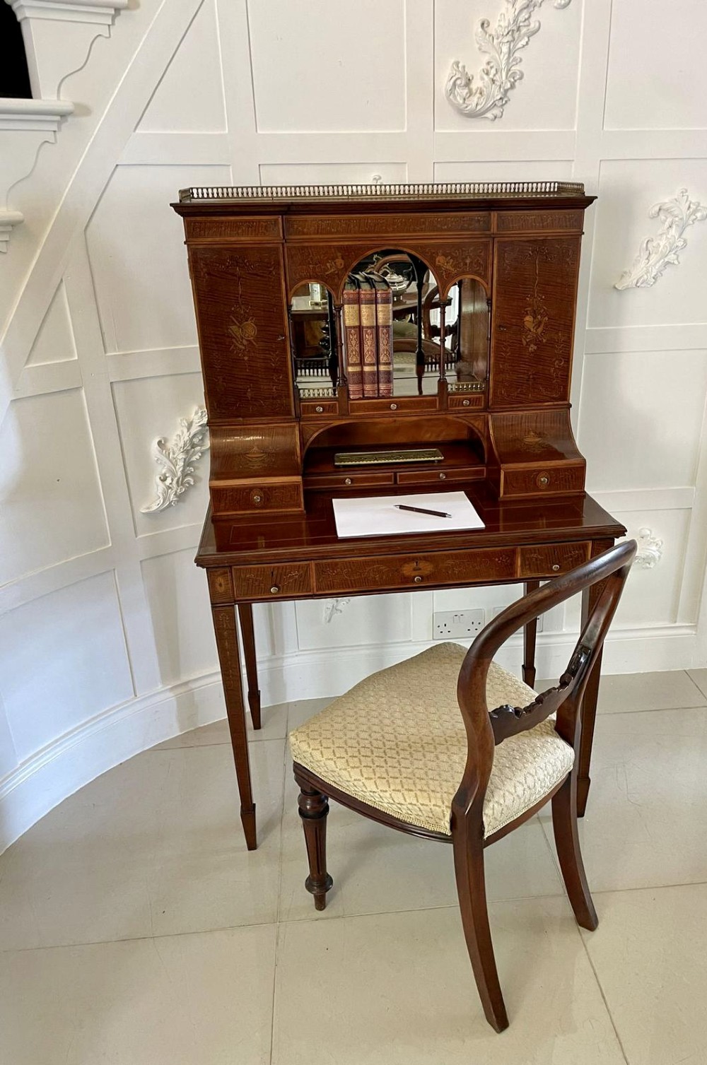 A Victorian inlaid mahogany writing desk featuring a brass gallery top, mirrored arched niche, floral marquetry cabinets, small drawers, and tapered square legs. View V
