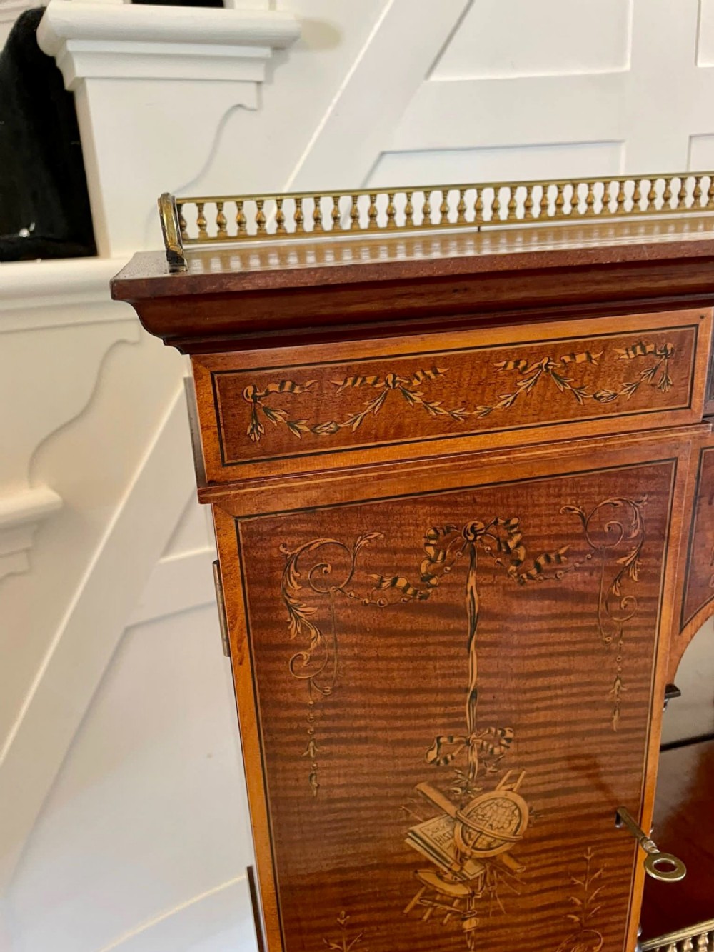 A Victorian inlaid mahogany writing desk featuring a brass gallery top, mirrored arched niche, floral marquetry cabinets, small drawers, and tapered square legs. View XIV