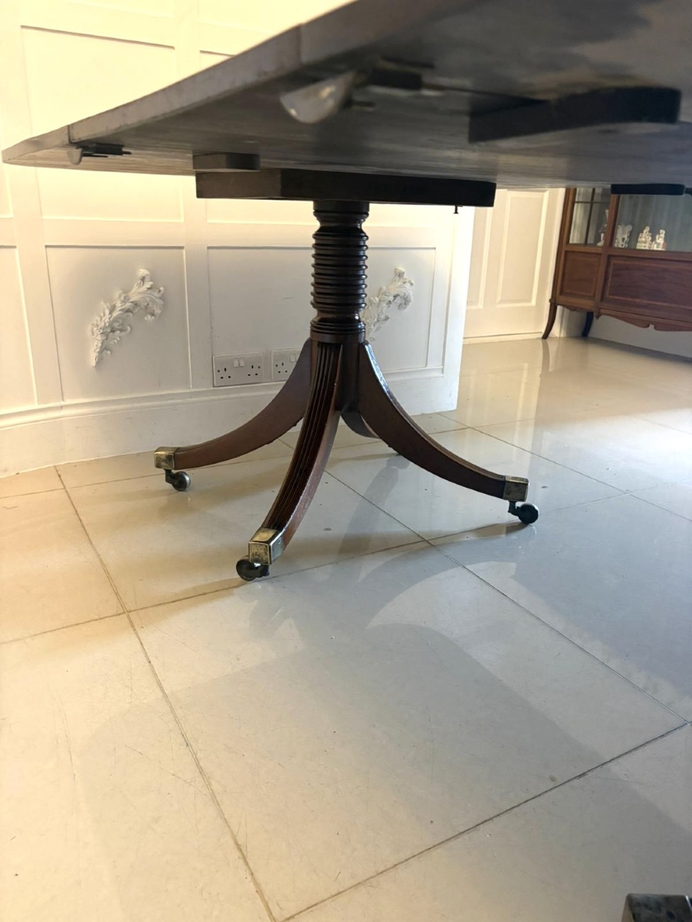 A large Georgian extending dining table crafted from polished figured mahogany with a three-pillar tripod pedestal base and brass castors. View VIII
