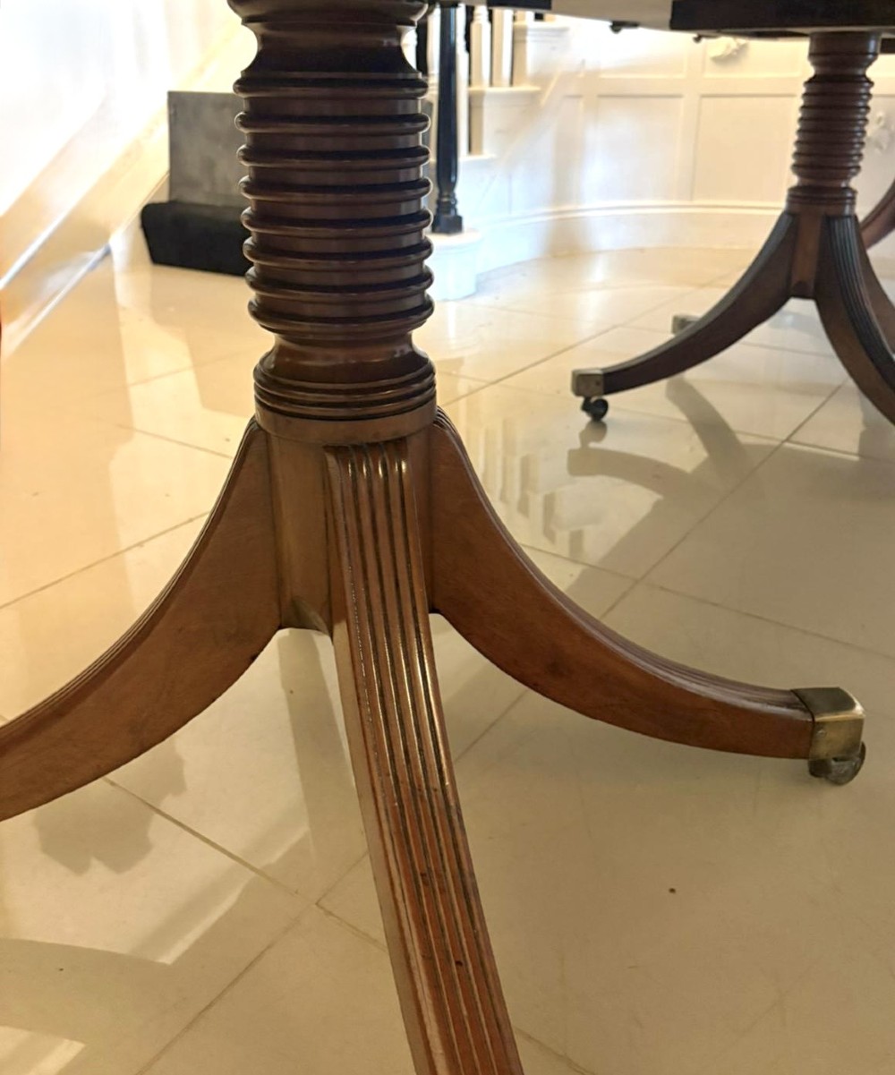 A large Georgian extending dining table crafted from polished figured mahogany with a three-pillar tripod pedestal base and brass castors. View X