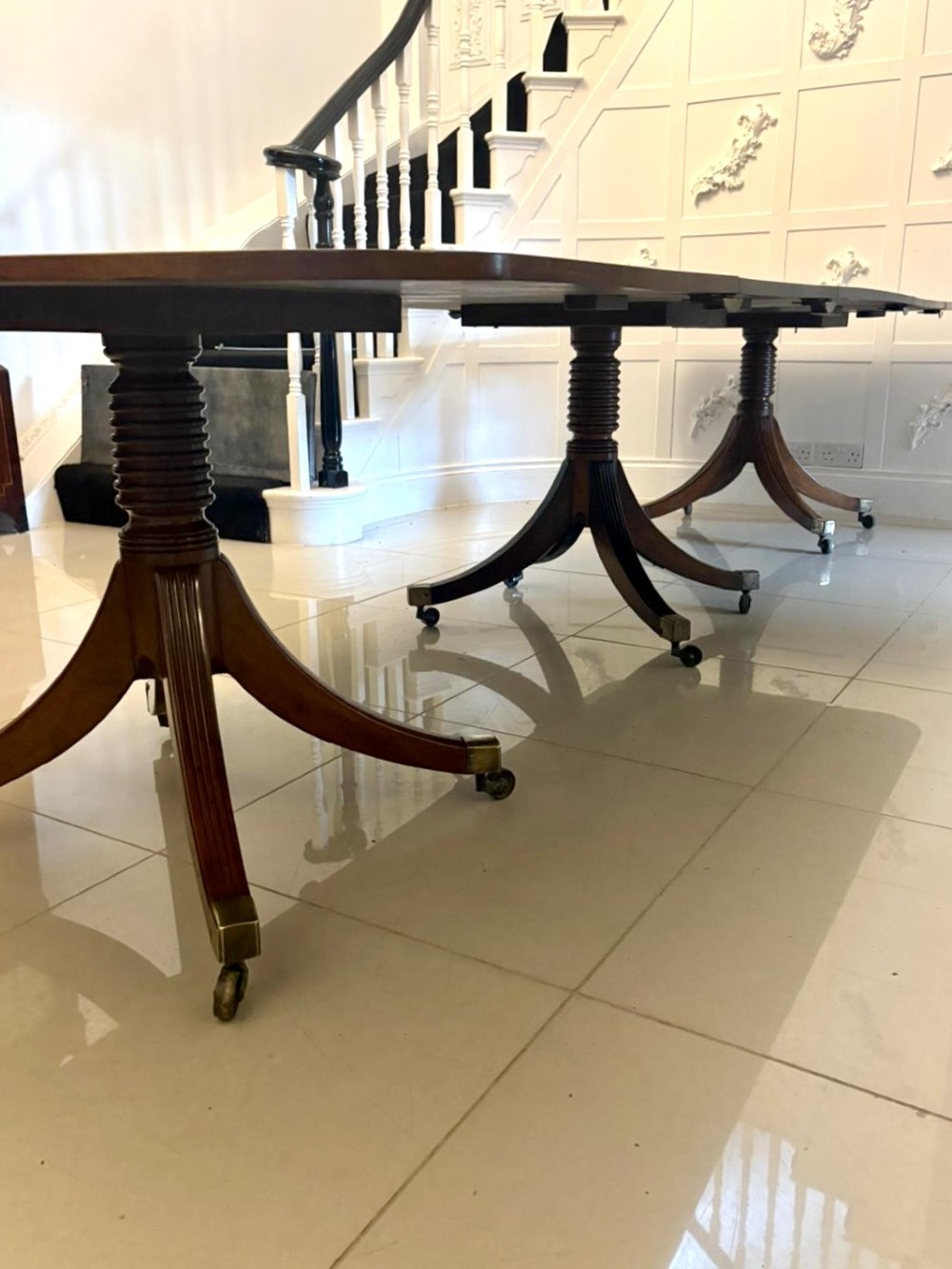 A large Georgian extending dining table crafted from polished figured mahogany with a three-pillar tripod pedestal base and brass castors. View XI