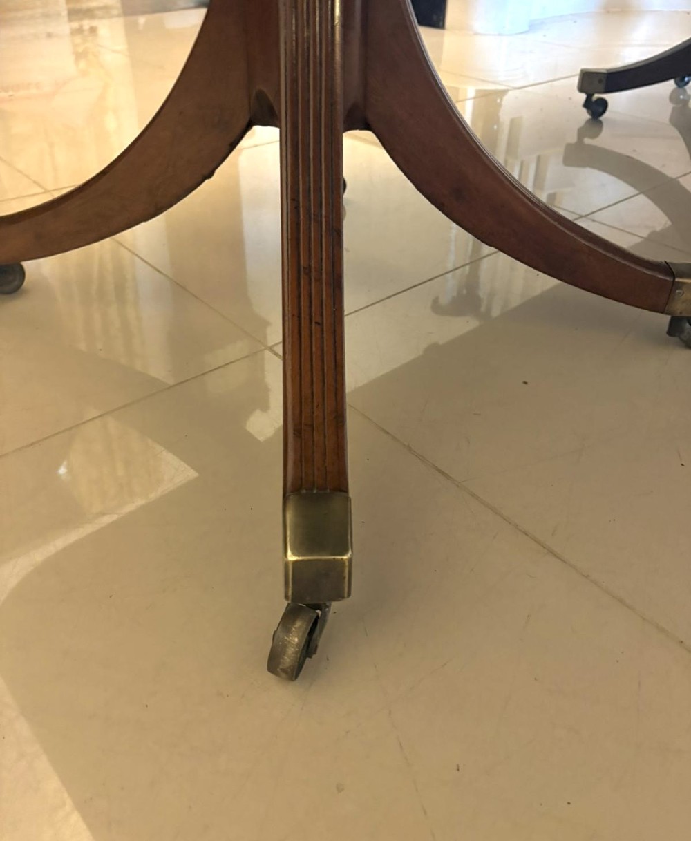 A large Georgian extending dining table crafted from polished figured mahogany with a three-pillar tripod pedestal base and brass castors. View XII