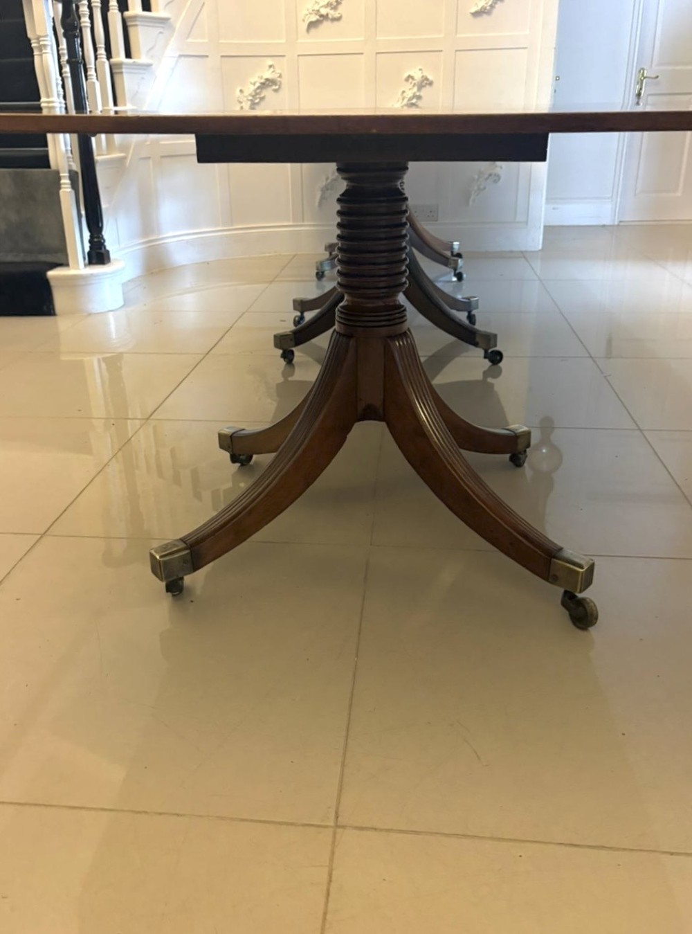 A large Georgian extending dining table crafted from polished figured mahogany with a three-pillar tripod pedestal base and brass castors. View XIII