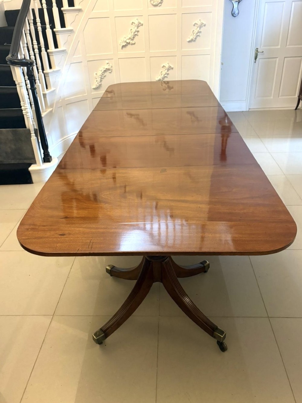 A large Georgian extending dining table crafted from polished figured mahogany with a three-pillar tripod pedestal base and brass castors.