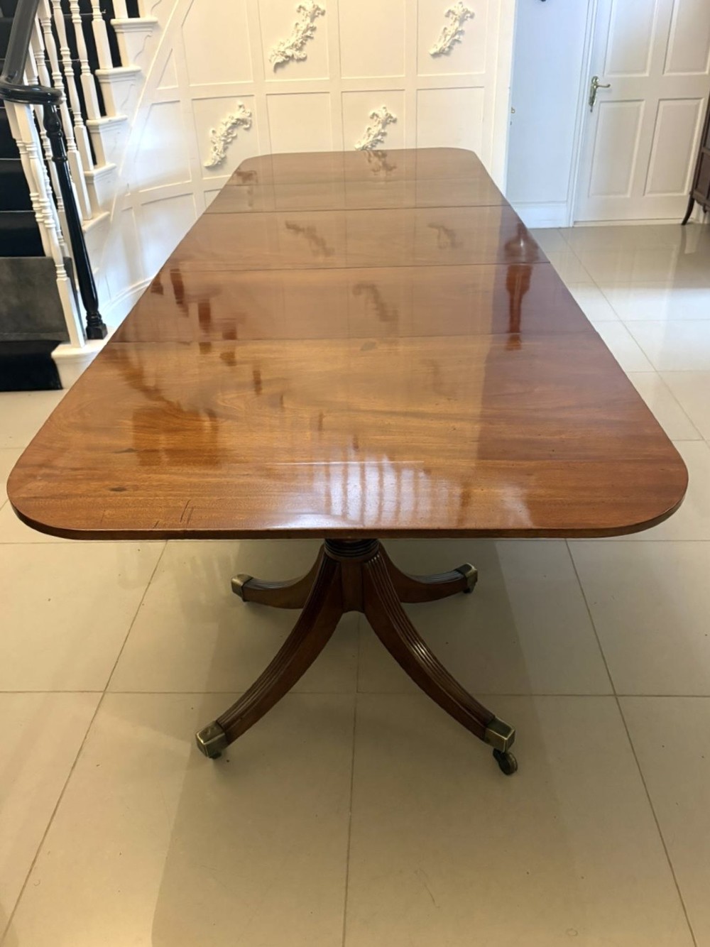 A large Georgian extending dining table crafted from polished figured mahogany with a three-pillar tripod pedestal base and brass castors. View XIV