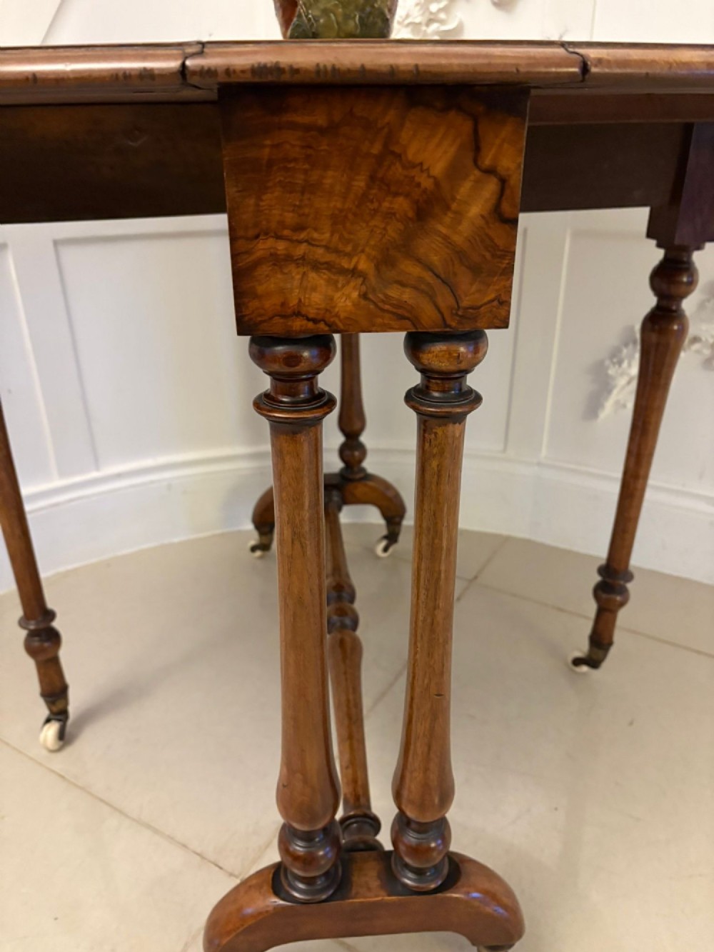 A folded Victorian burr walnut Sutherland table featuring turned upright supports, a stretcher base, and white ceramic castors. View III