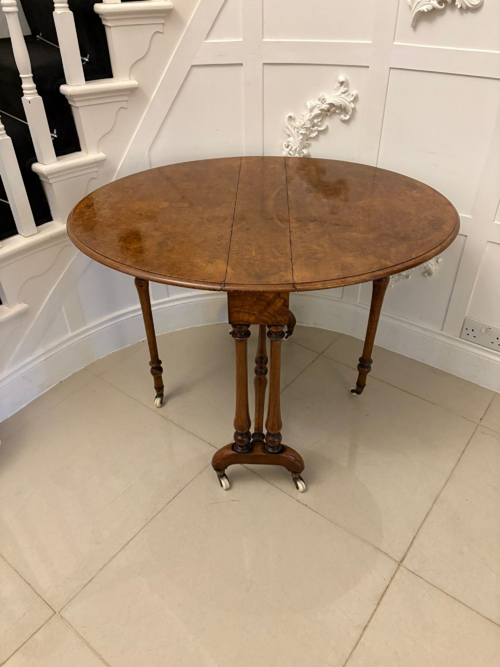 A folded Victorian burr walnut Sutherland table featuring turned upright supports, a stretcher base, and white ceramic castors. View IV