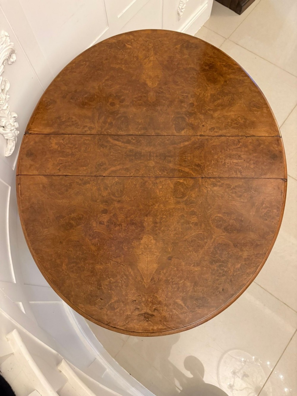 A folded Victorian burr walnut Sutherland table featuring turned upright supports, a stretcher base, and white ceramic castors. View V