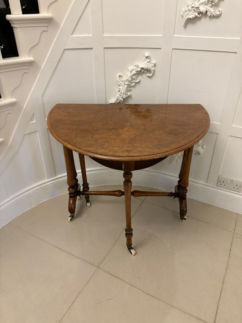 A folded Victorian burr walnut Sutherland table featuring turned upright supports, a stretcher base, and white ceramic castors. View VI
