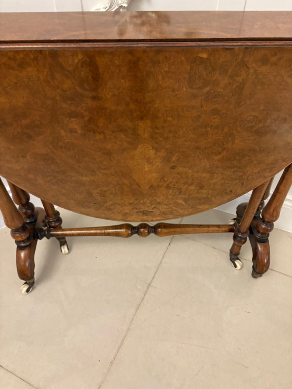 A folded Victorian burr walnut Sutherland table featuring turned upright supports, a stretcher base, and white ceramic castors. View VII