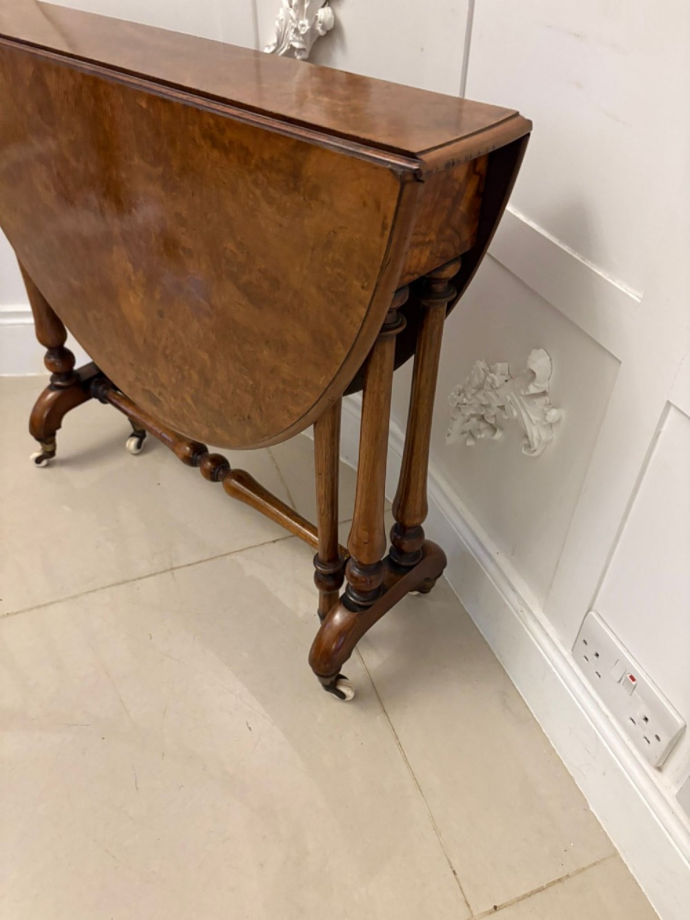 A folded Victorian burr walnut Sutherland table featuring turned upright supports, a stretcher base, and white ceramic castors. View IX