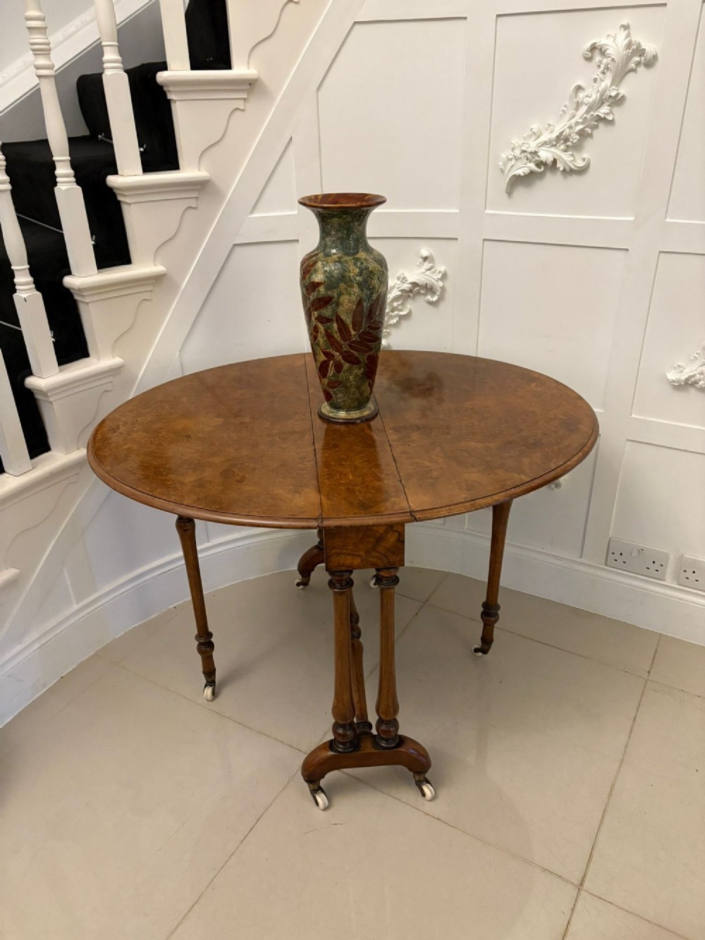 A folded Victorian burr walnut Sutherland table featuring turned upright supports, a stretcher base, and white ceramic castors. View X