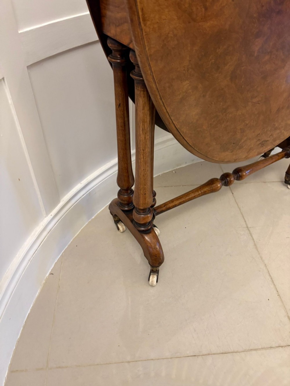 A folded Victorian burr walnut Sutherland table featuring turned upright supports, a stretcher base, and white ceramic castors. View XII