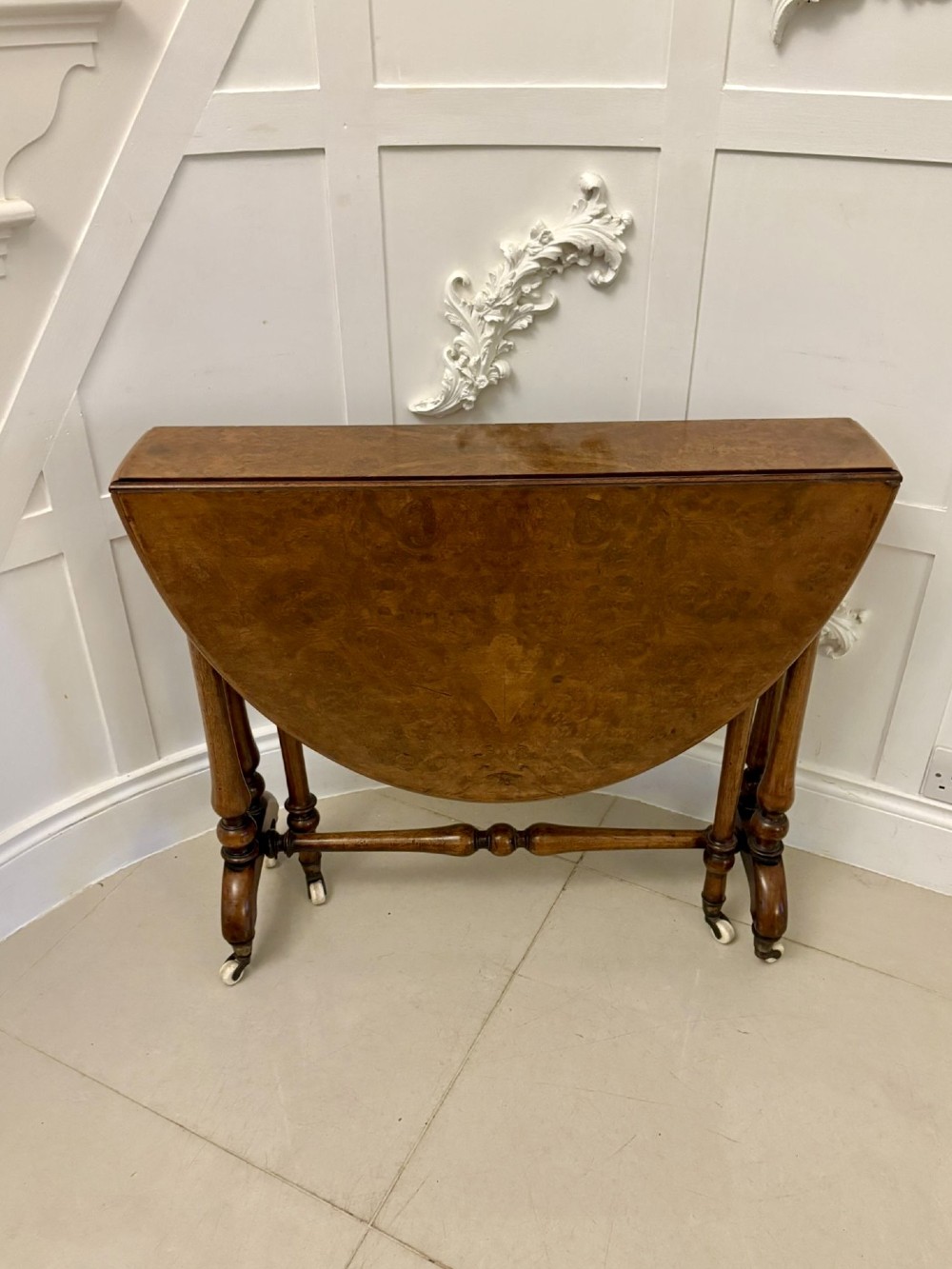 A folded Victorian burr walnut Sutherland table featuring turned upright supports, a stretcher base, and white ceramic castors.