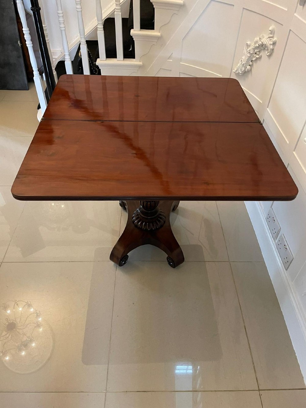 A William IV mahogany fold-over tea table with a turned gadrooned pedestal stem and a concave quadform base ending in scroll feet. View II