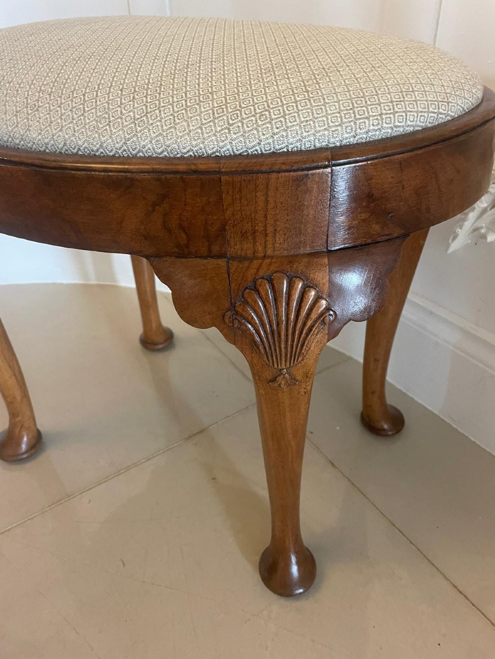 An antique oval walnut stool featuring shell-carved cabriole legs, pad feet, and a geometric pattern upholstered seat. View II