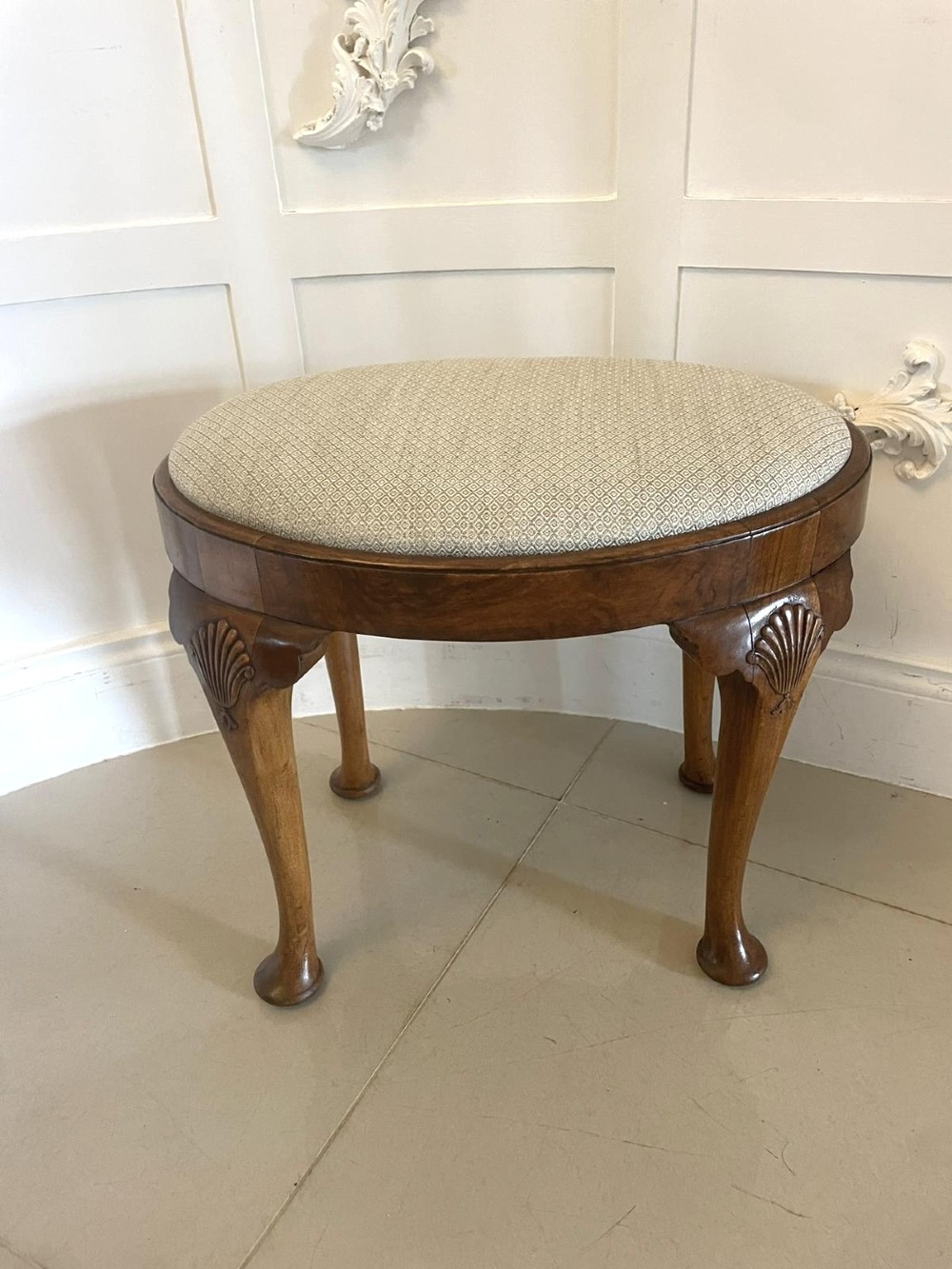 An antique oval walnut stool featuring shell-carved cabriole legs, pad feet, and a geometric pattern upholstered seat.
