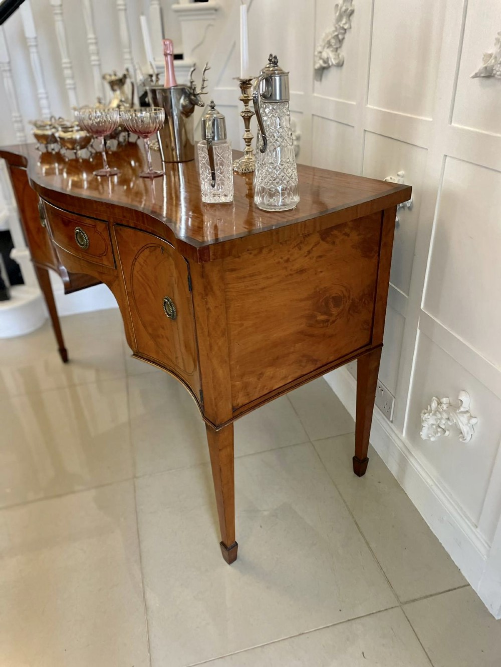 An antique satinwood serpentine-front sideboard featuring oval inlay panels, brass ring handles, and tapered square legs. View VIII