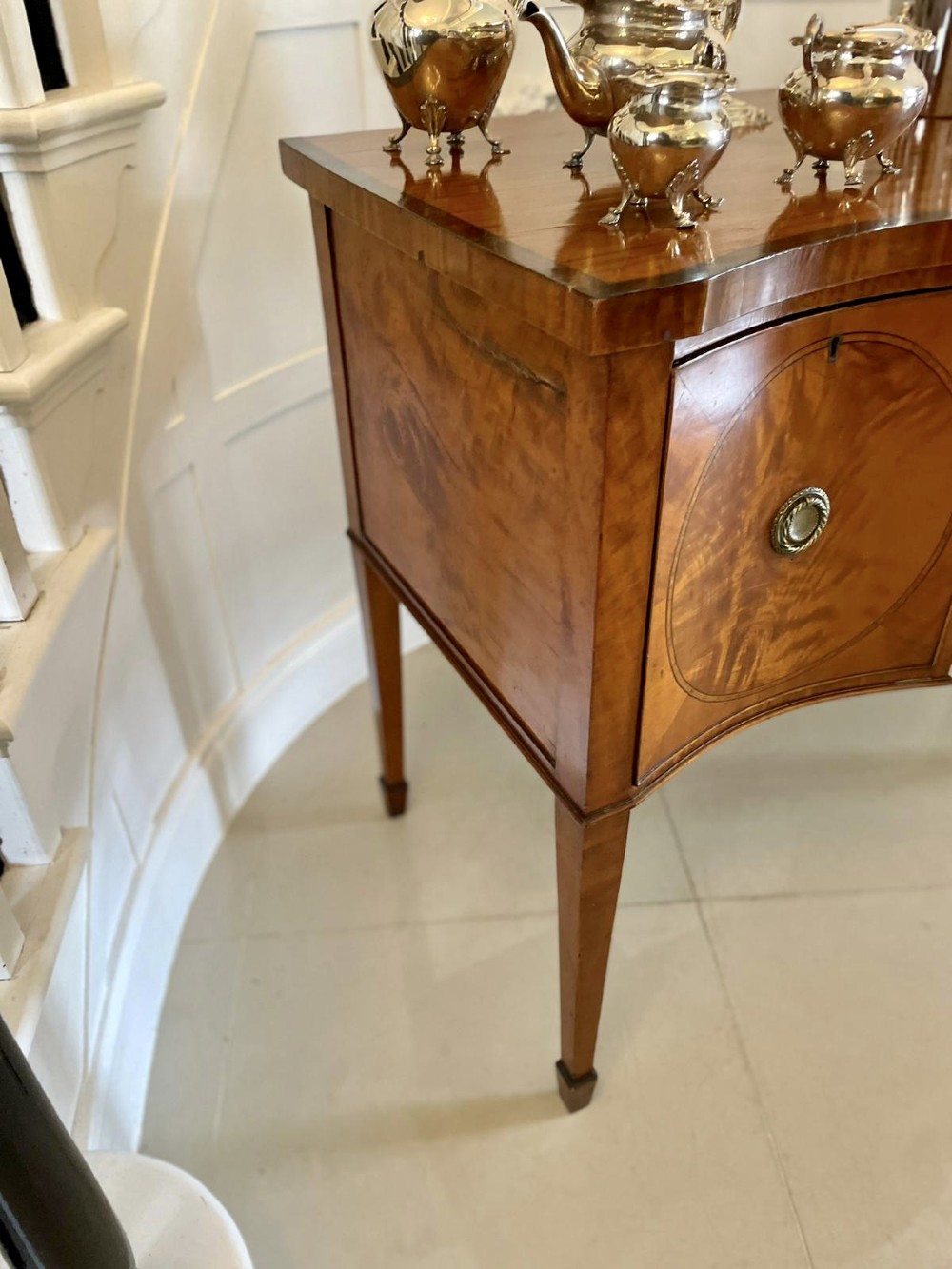 An antique satinwood serpentine-front sideboard featuring oval inlay panels, brass ring handles, and tapered square legs. View IX