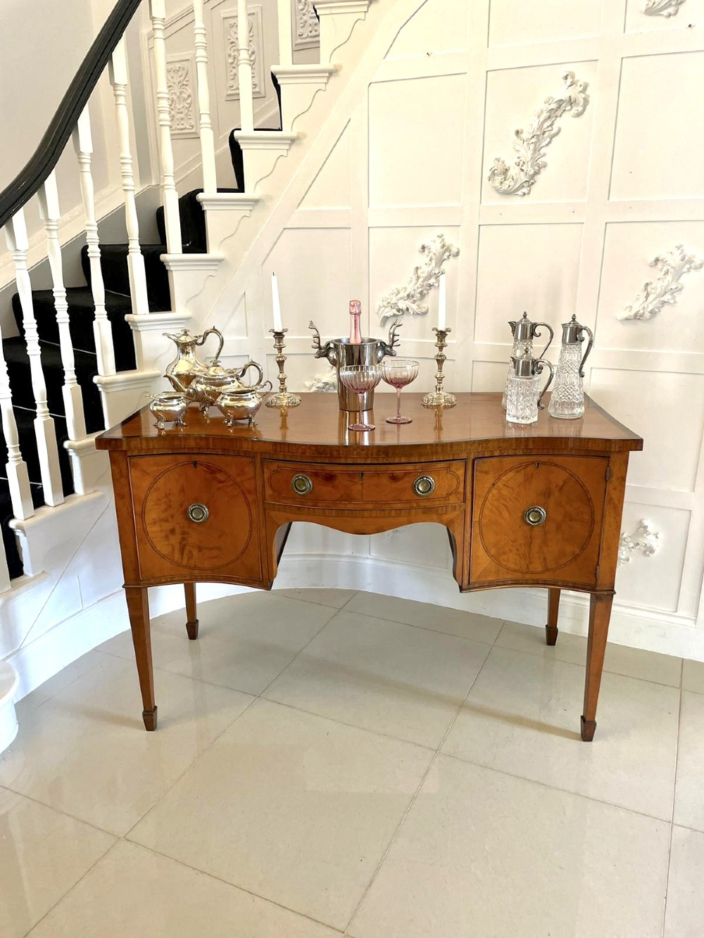 An antique satinwood serpentine-front sideboard featuring oval inlay panels, brass ring handles, and tapered square legs. View XII