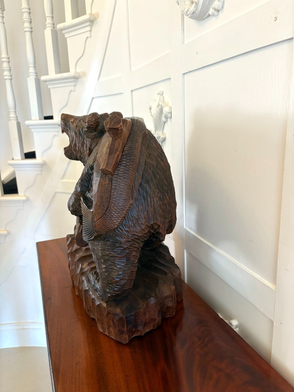 A hand-carved dark linden wood sculpture depicting a roaring bear carrying a fish over its back, positioned on a carved textured base. View III