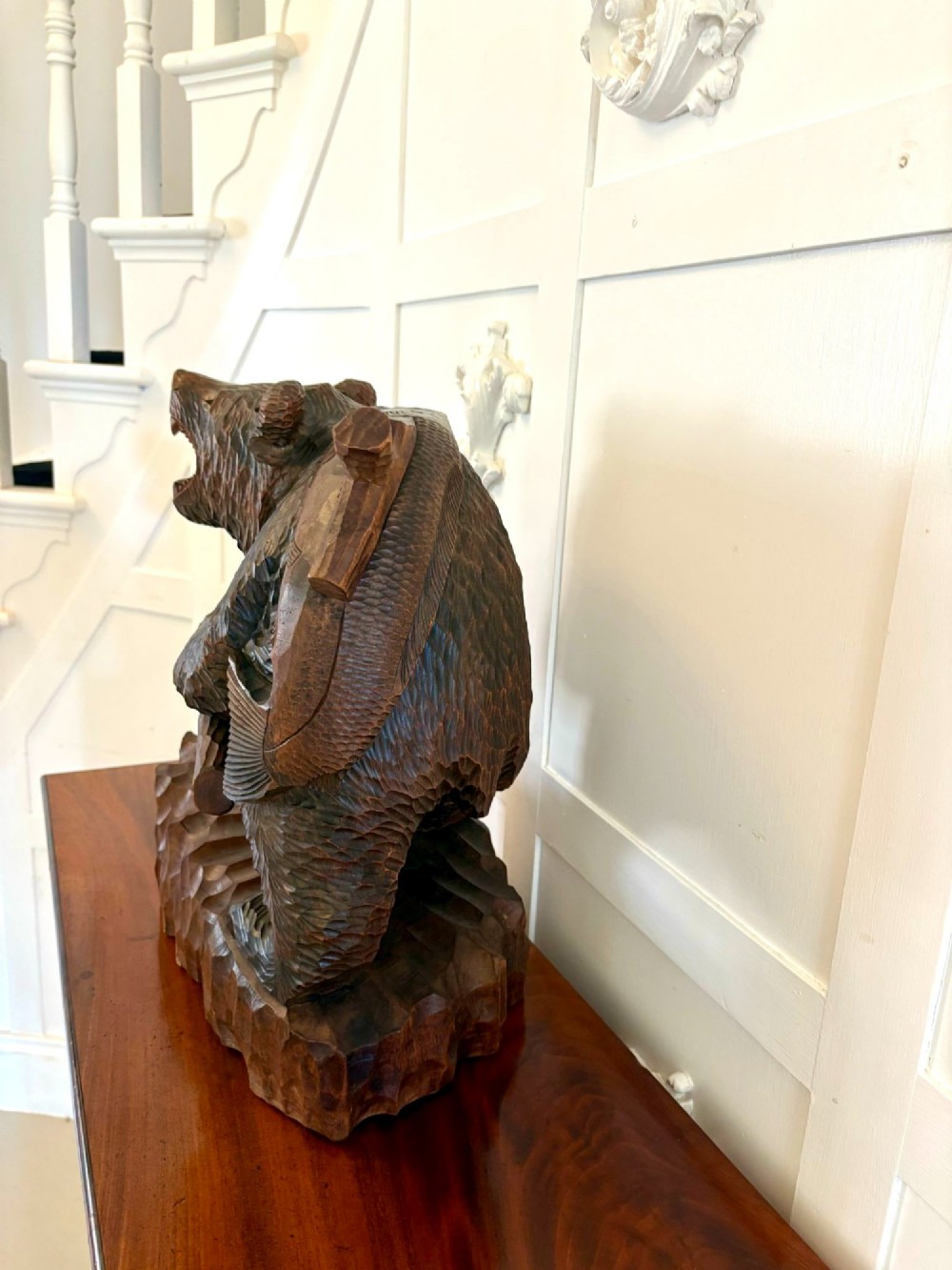 A hand-carved dark linden wood sculpture depicting a roaring bear carrying a fish over its back, positioned on a carved textured base. View IV