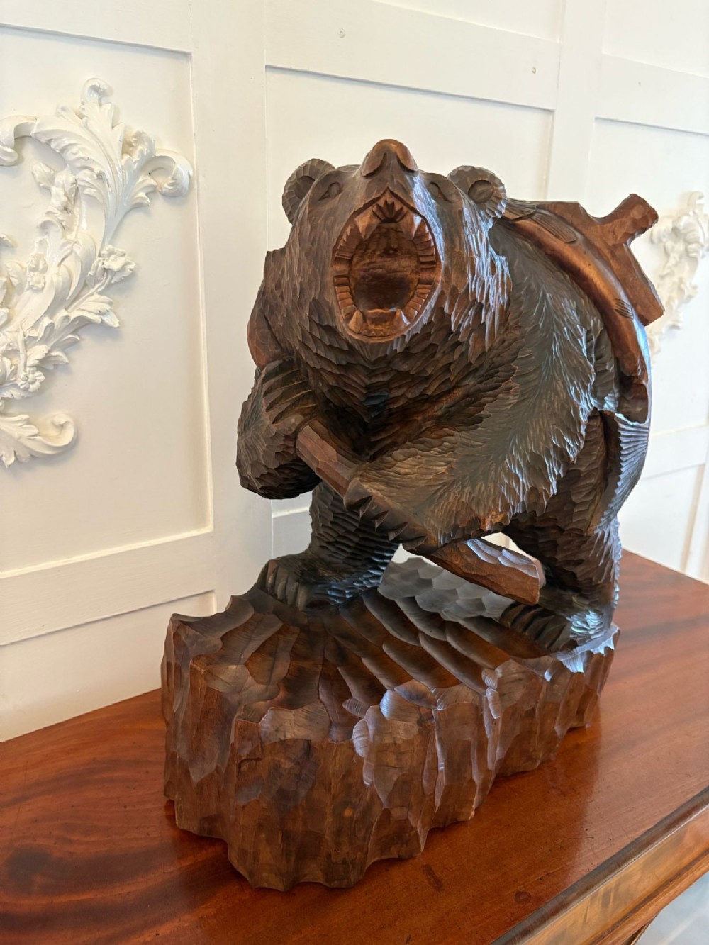 A hand-carved dark linden wood sculpture depicting a roaring bear carrying a fish over its back, positioned on a carved textured base. View VII