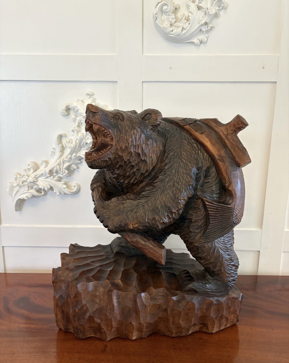 A hand-carved dark linden wood sculpture depicting a roaring bear carrying a fish over its back, positioned on a carved textured base. View IX