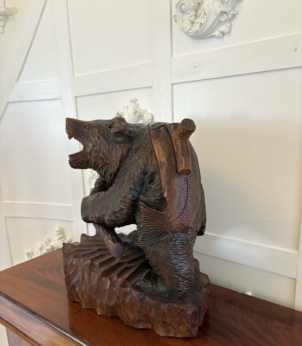 A hand-carved dark linden wood sculpture depicting a roaring bear carrying a fish over its back, positioned on a carved textured base. View XIII