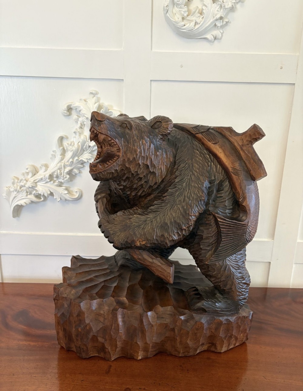 A hand-carved dark linden wood sculpture depicting a roaring bear carrying a fish over its back, positioned on a carved textured base.