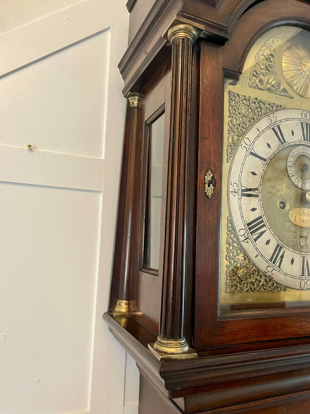 A George III mahogany longcase clock featuring an arched brass dial, urn finials, and an arched trunk door. View V