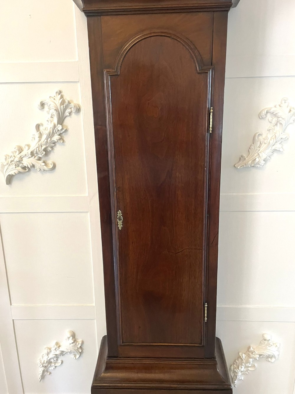 A George III mahogany longcase clock featuring an arched brass dial, urn finials, and an arched trunk door. View VI