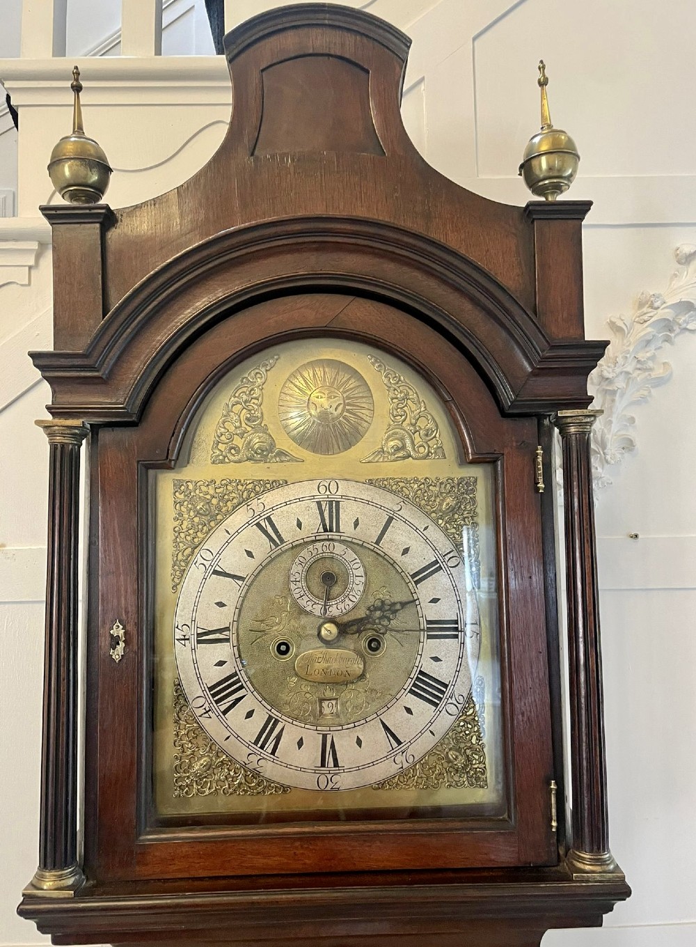 A George III mahogany longcase clock featuring an arched brass dial, urn finials, and an arched trunk door. View XV