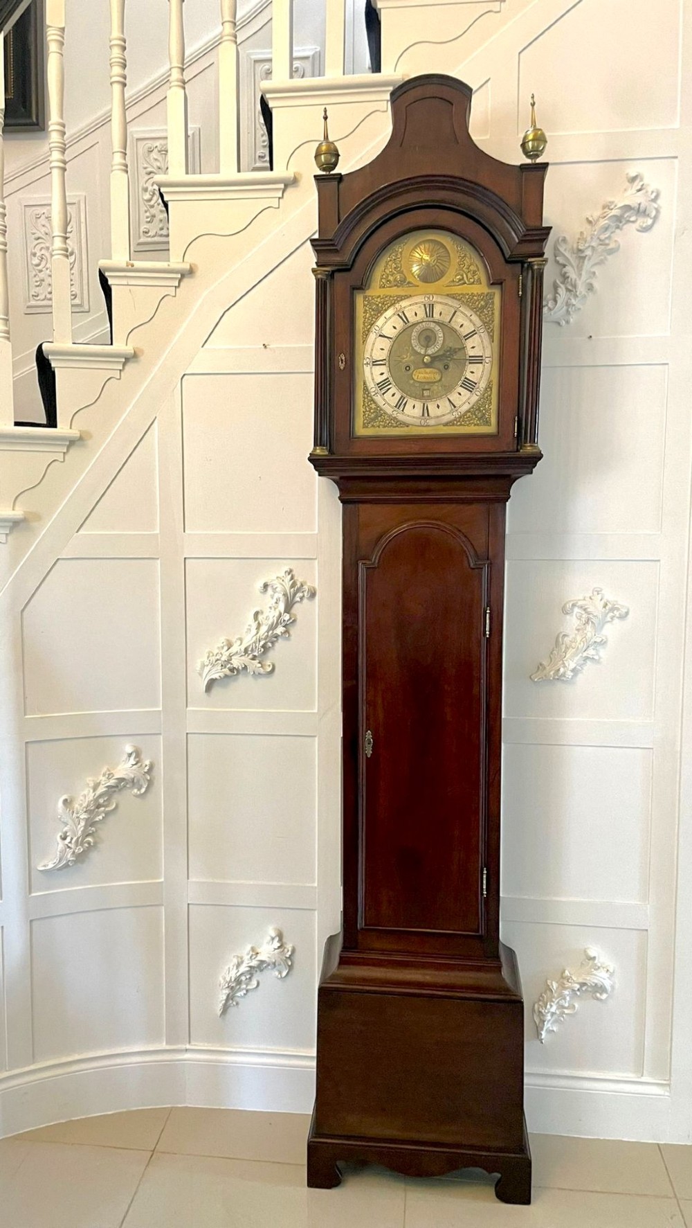 A George III mahogany longcase clock featuring an arched brass dial, urn finials, and an arched trunk door.