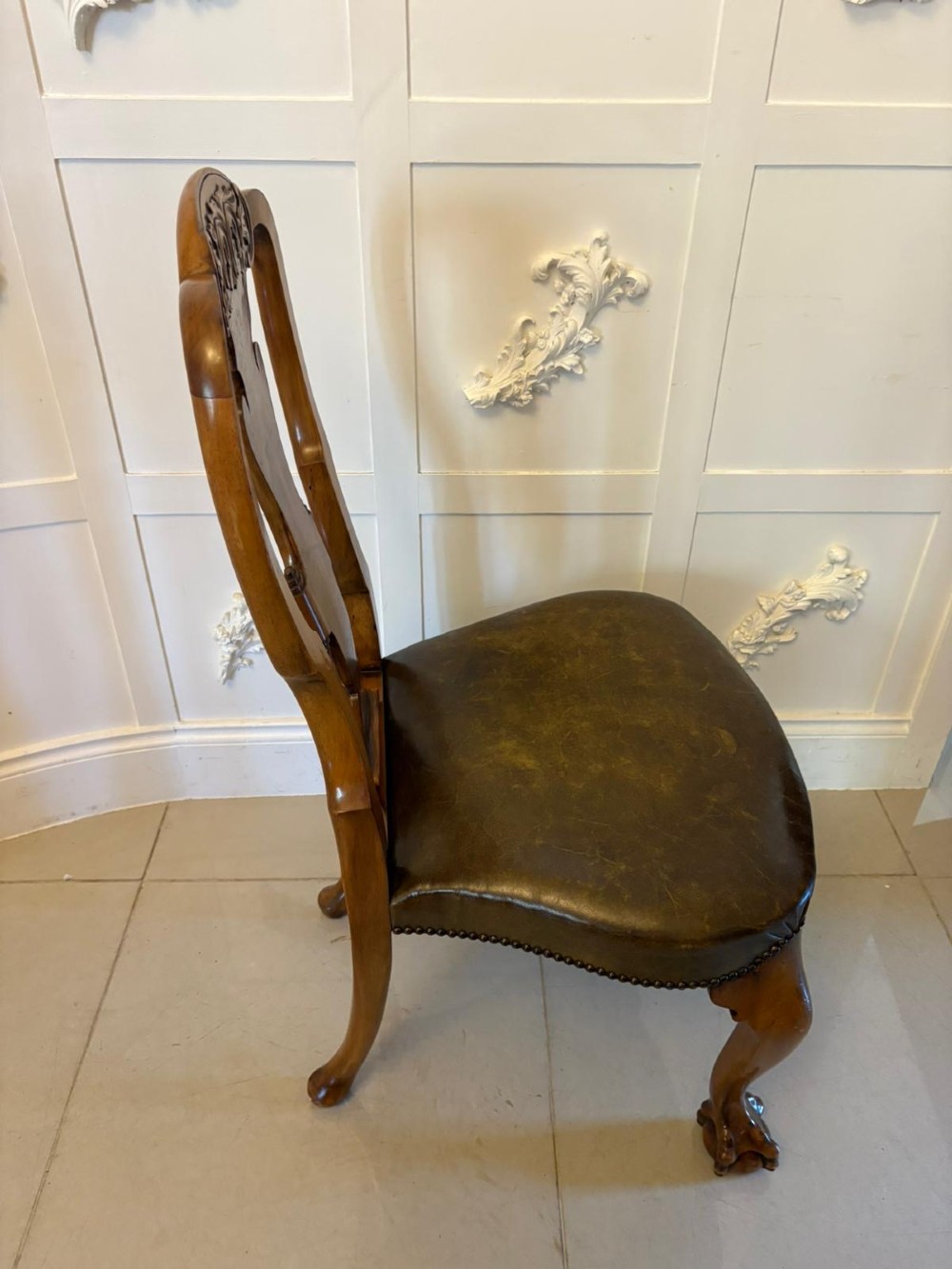 A set of six carved walnut dining chairs featuring decorative back splats, leather seats with brass studs, cabriole legs, and ball and claw feet. View XIII