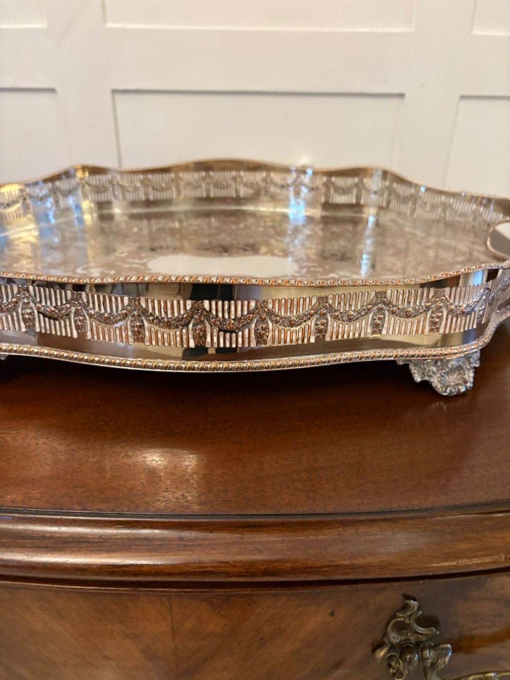 A silver-plated Edwardian tea tray featuring an engraved surface, a pierced gallery border with integrated handles, and cast feet. View VI
