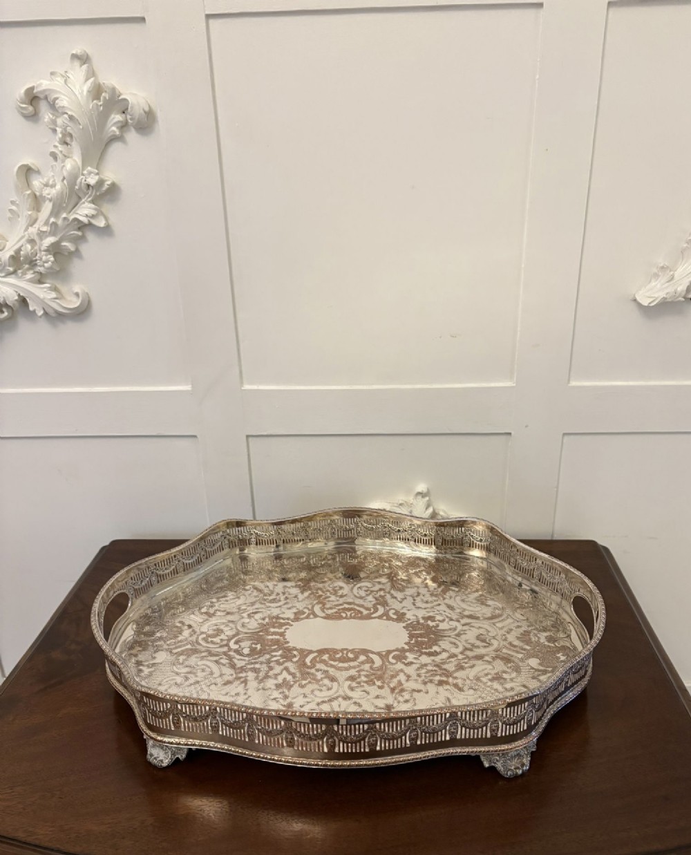 A silver-plated Edwardian tea tray featuring an engraved surface, a pierced gallery border with integrated handles, and cast feet.