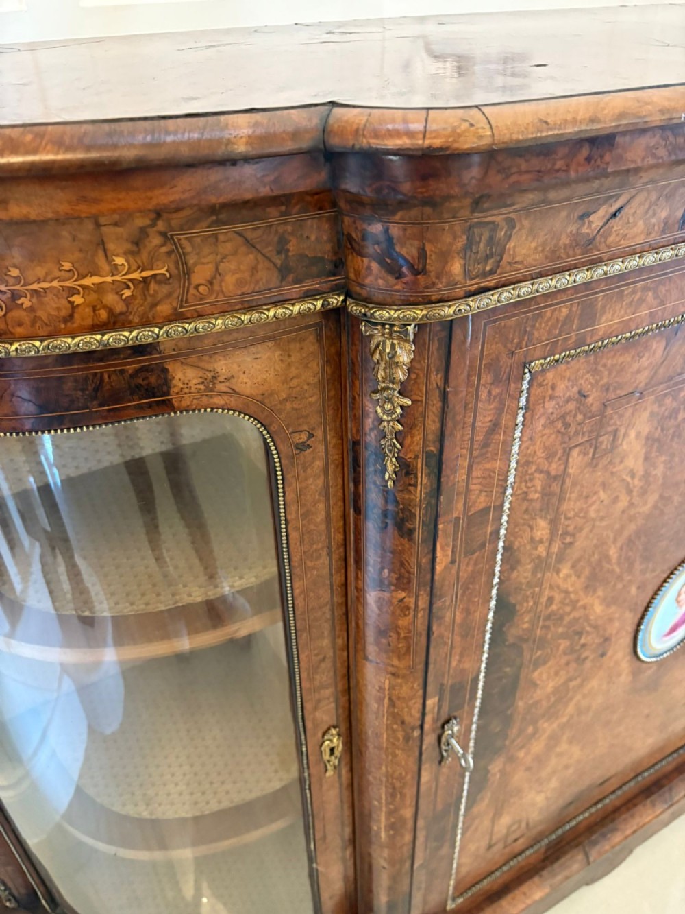 A Victorian burr walnut credenza featuring a central door with a hand-painted porcelain portrait plaque flanked by two curved glass display cupboards and gilt-brass mounts. View VII