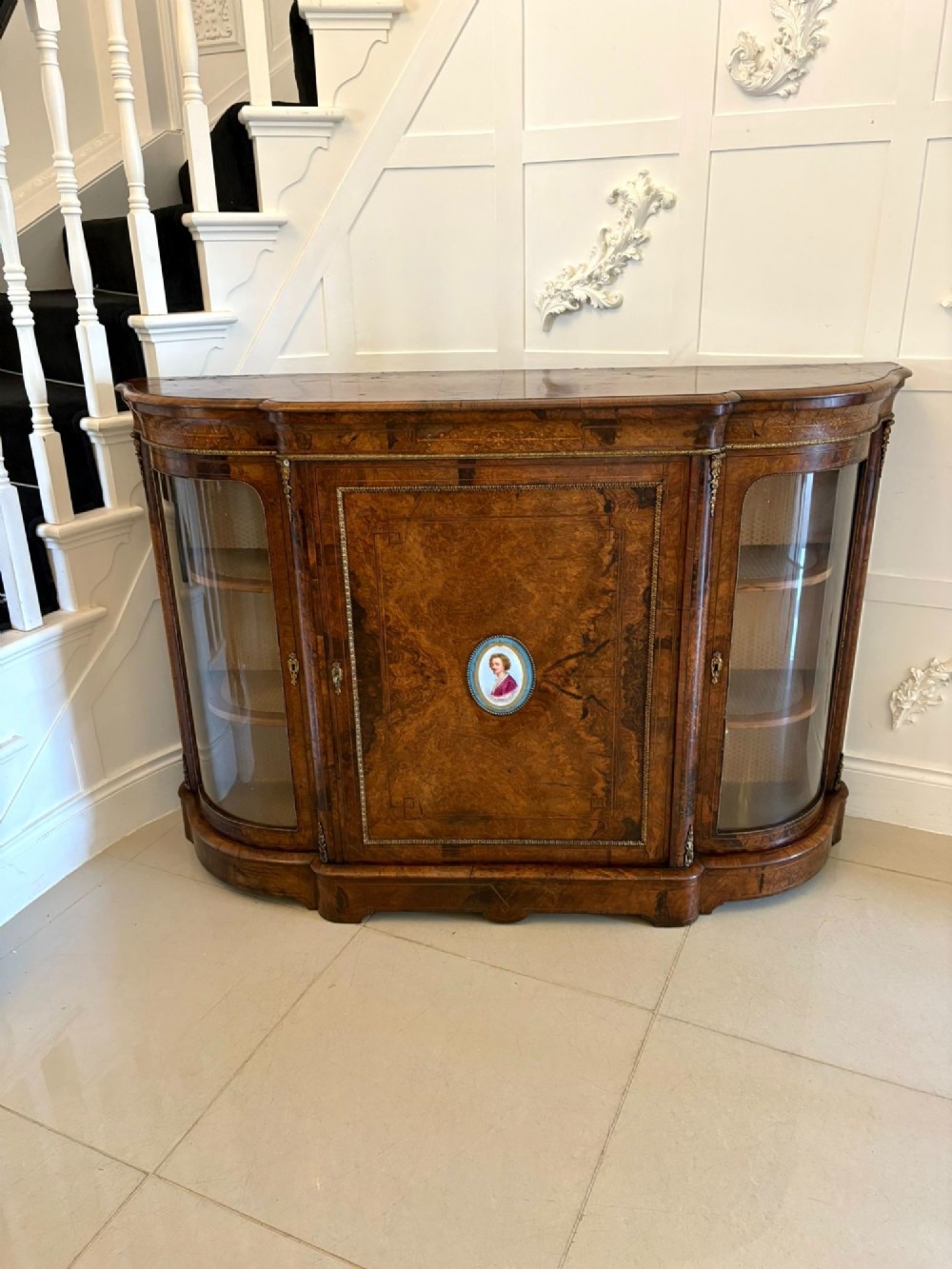 A Victorian burr walnut credenza featuring a central door with a hand-painted porcelain portrait plaque flanked by two curved glass display cupboards and gilt-brass mounts.