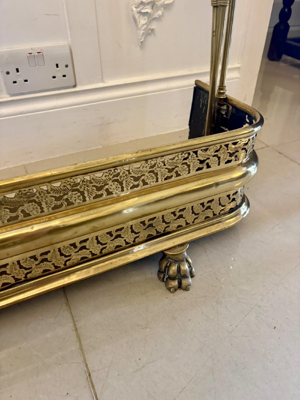 An antique Regency period brass fireplace fender featuring intricate pierced metalwork, claw feet, and matching original brass fire irons positioned at either end. View II