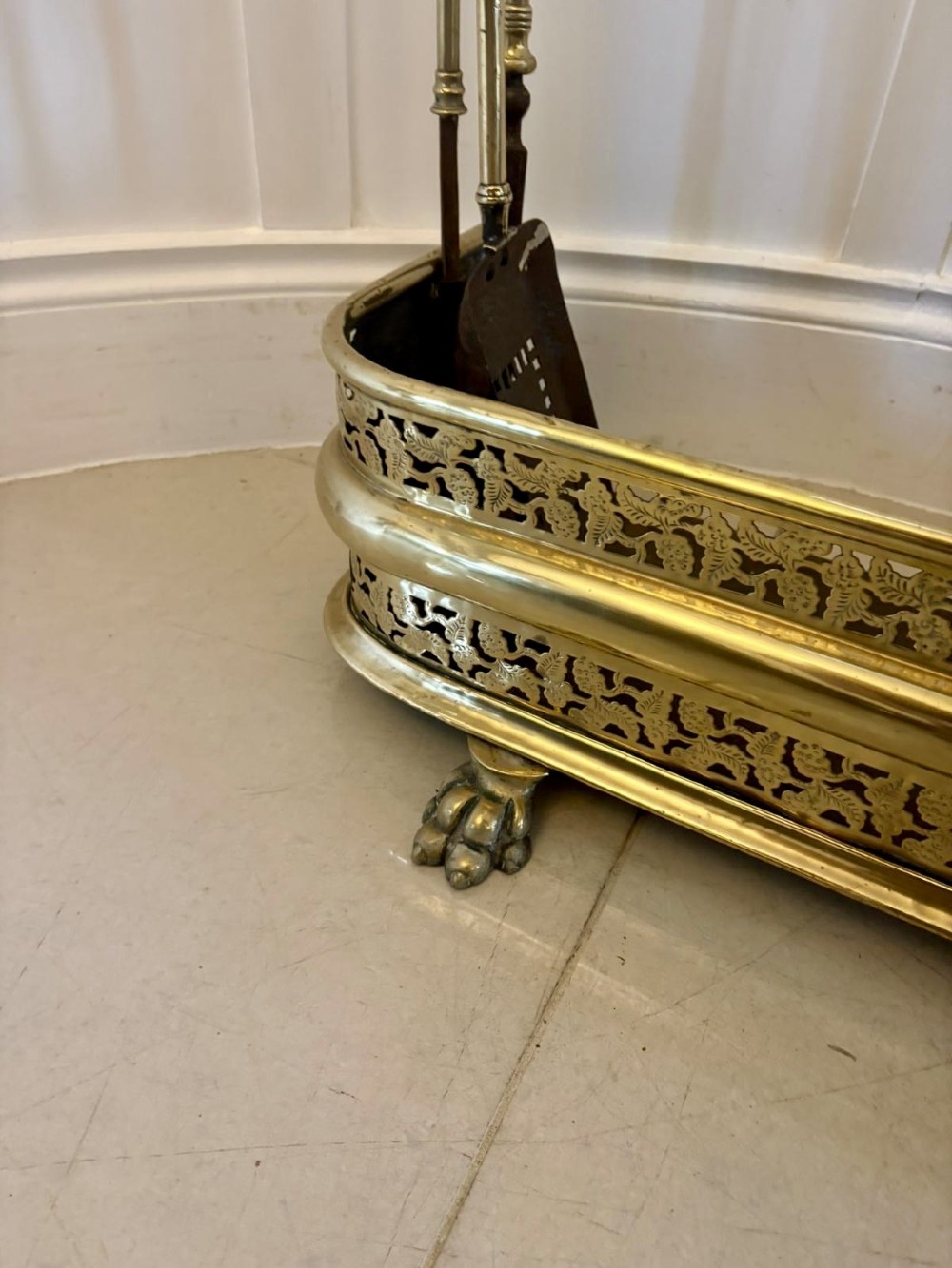An antique Regency period brass fireplace fender featuring intricate pierced metalwork, claw feet, and matching original brass fire irons positioned at either end. View III